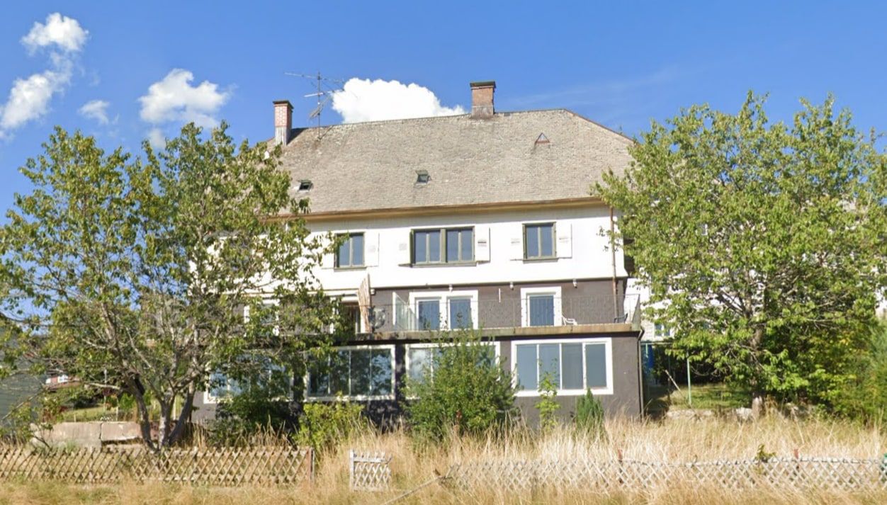 Zweigeschossiges Bestandsgebäude mit Satteldach vor der Sanierung, davor ein verwilderter Garten